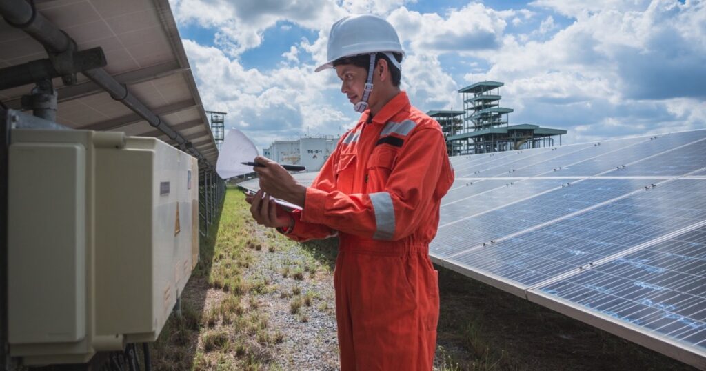 Technician in orange workwear checking an electrical cabinet at a solar park