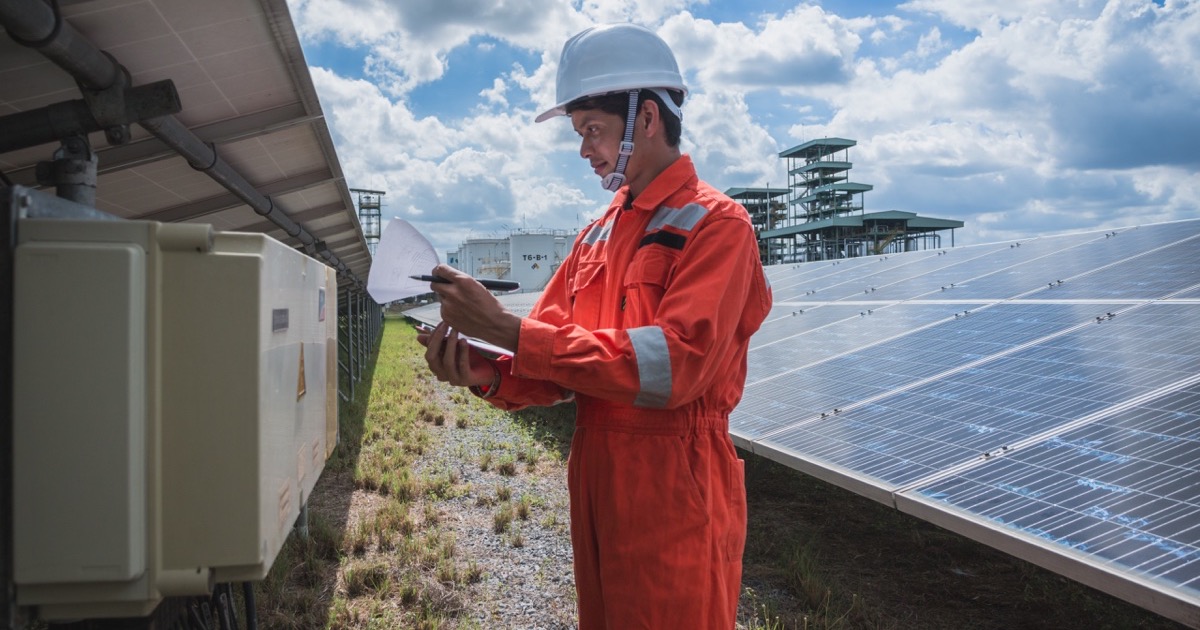 Technician in orange workwear checking an electrical cabinet at a solar park
