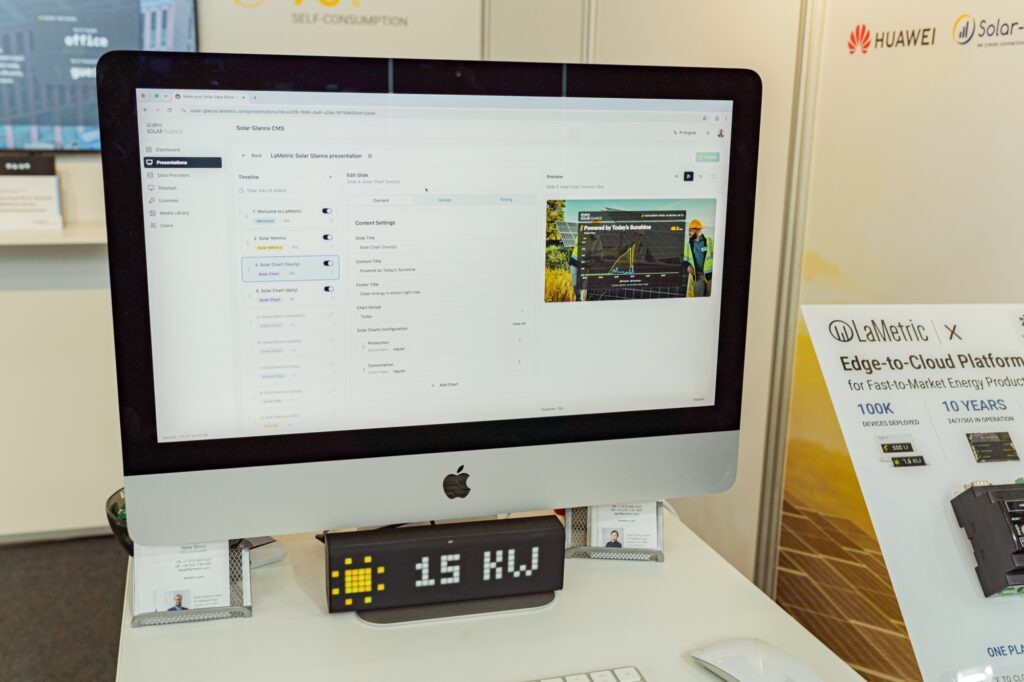 Solar Glance CMS open on an iMac at a trade show booth, with a LaMetric TIME showing 15 kW in front