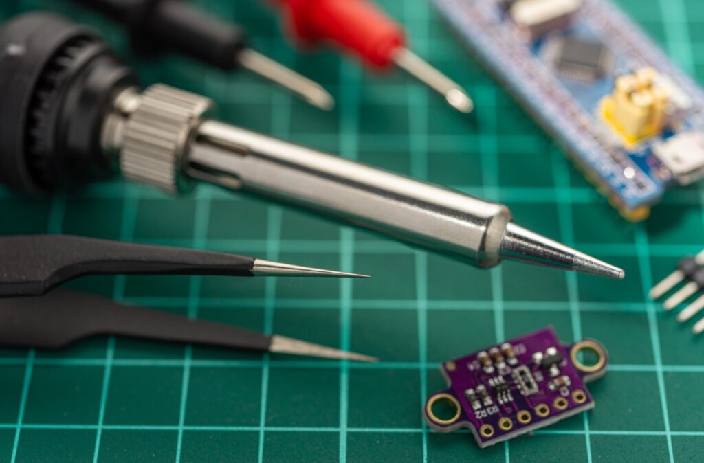 Soldering iron, tweezers and a small development board on a cutting mat
