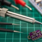 Soldering iron, tweezers and a small development board on a cutting mat