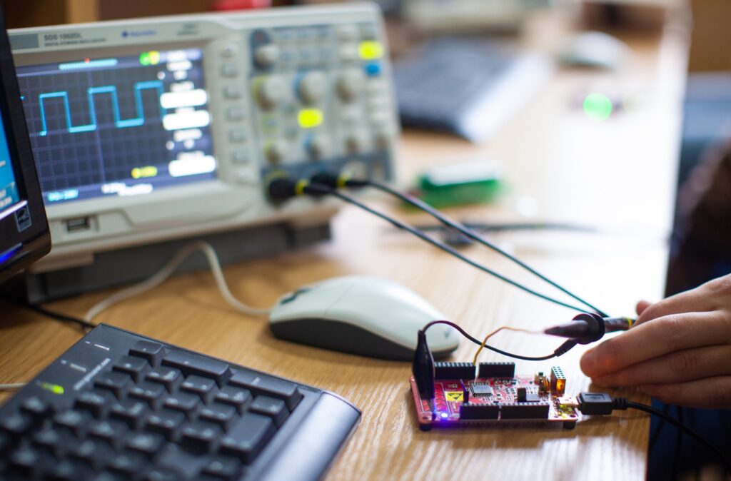 Microcontroller board connected to an oscilloscope on an engineer's desk