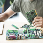Male technician repairing motherboard using laptop